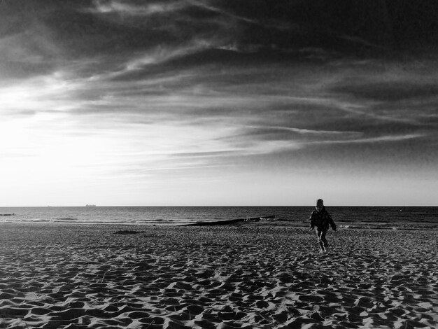 Foto largura completa de un niño corriendo por la playa contra el cielo