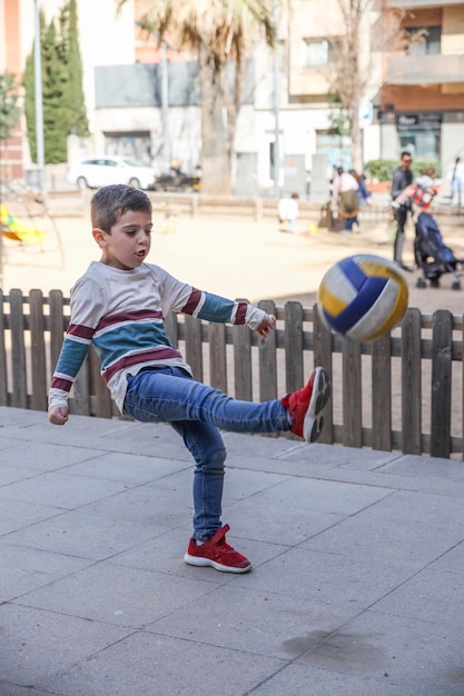 Foto largura completa de un niño lindo jugando con la pelota en la acera