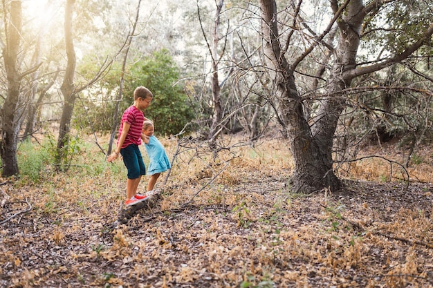 Largura completa de niño y niña caminando en árbol caído