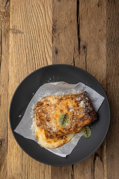 Lasagna de Bolonia en un plato negro en una mesa de madera