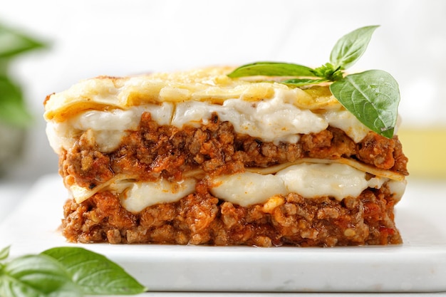 Lasagne Hausgemachte italienische Lasagne mit Bolognese-Fleischsoße Bechamelkäse und Basilikum auf weißem Brett