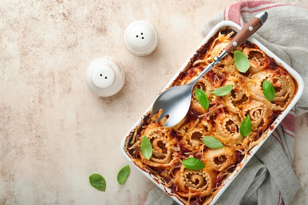 Lasaña Lasaña casera pasta rotolo horneada con salsa de tomate queso crema y albahaca en sartén blanco sobre piedra de pizarra clara o fondo de hormigón Concepto de cocina italiana Vista superior con espacio de copia