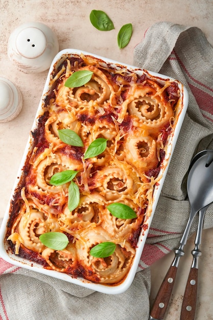 Lasaña Lasaña casera pasta rotolo horneada con salsa de tomate queso crema y albahaca en sartén blanco sobre piedra de pizarra clara o fondo de hormigón Concepto de cocina italiana Vista superior con espacio de copia