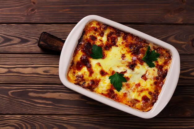 Lasaña con queso en una bandeja para hornear, sobre una mesa de madera