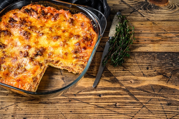 Lasaña con salsa boloñesa y carne picada en una fuente para horno. Fondo de madera. Vista superior. Copie el espacio.