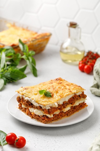 Lasaña con salsa boloñesa de carne y queso sobre plato blanco y fondo gris