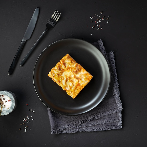 Lasanha de carne fresca em um prato preto sobre fundo preto de concreto vista superior comida italiana