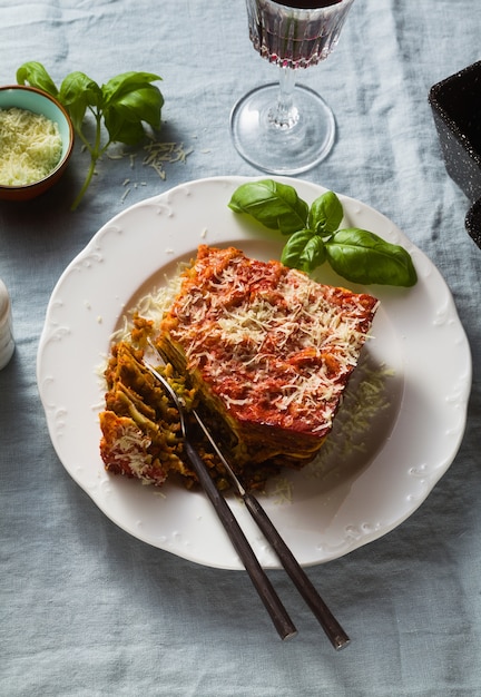 Lasanha vegana com lentilhas e ervilhas verdes em uma assadeira sobre uma mesa com uma toalha de mesa de linho azul. e vinho tinto em copos