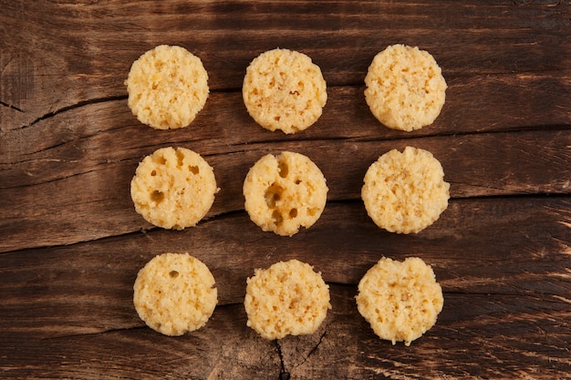 Foto lascas de queijo crocante em fundo de madeira marrom.