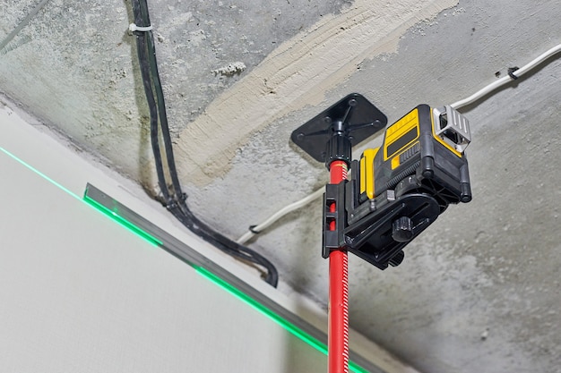 Laser-Level-Messgerät mit sichtbarem grünem Laserstrahl an der Wand auf der Baustelle. Füllstand messen. Professionelle Ausrüstung für die Installation von Spanndecken. Hausrenovierungskonzept, Nahaufnahme