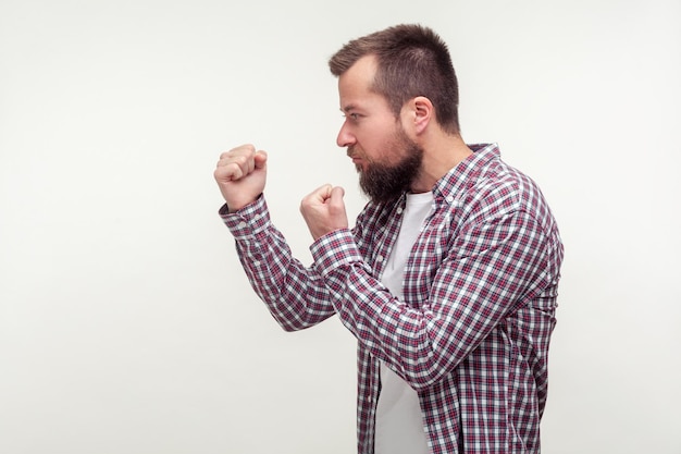 Lass uns kämpfen. Seitenansicht eines aggressiven bärtigen Mannes in lässigem kariertem Hemd, der mit erhobenen Fäusten steht, bereit zu schlagen, leerer Platz für Anzeigentext, Kopierraum. Indoor-Studioaufnahme isoliert auf weißem Hintergrund