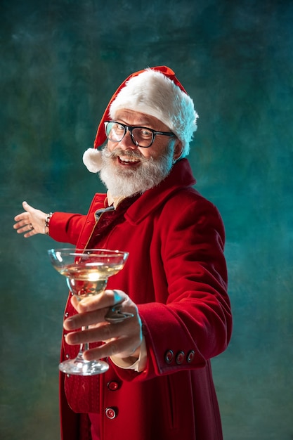 Lass uns Party machen. Moderner stilvoller Weihnachtsmann in rotem modischem Anzug und Cowboyhut auf dunklem Hintergrund. Sieht aus wie ein Rockstar. Silvester und Heiligabend, Feiern, Feiertage, Winterstimmung, Mode.