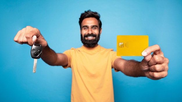 Lassen Sie Ihren Traum wahr werden. Aufgeregt zeigt ein indischer Mann einen neuen Autoschlüssel und eine Kreditkarte, die ein Auto kauft