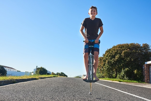 Lassen Sie uns hüpfen Ganzkörperporträt eines Jungen, der draußen auf einem Pogo-Stick hüpft