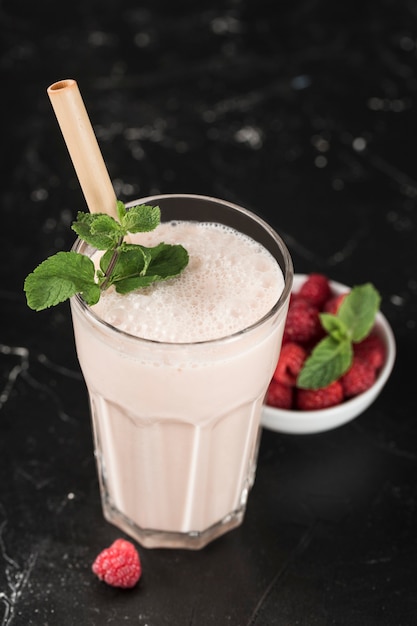 Lassi bebida com framboesas em um copo com hortelã e um tubo de bambu em um fundo escuro. Orientação vertical. Bebida refrescante tradicional indiana.