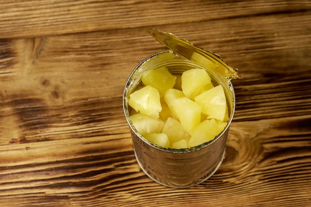 Lata aberta com pedaços de abacaxi na mesa de madeira