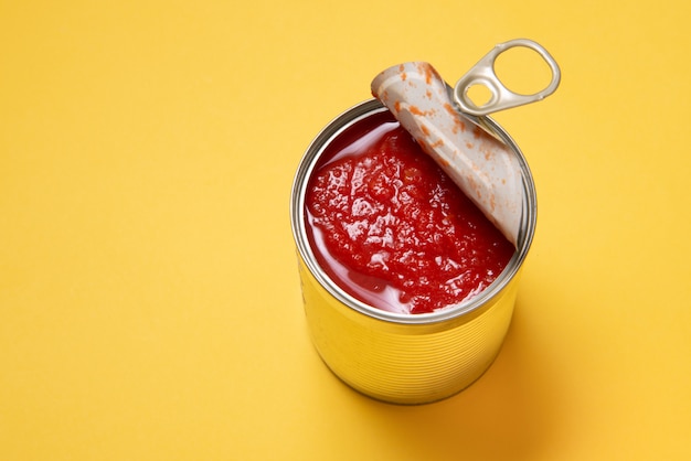 Lata aberta com tomates enlatados, sobre fundo amarelo