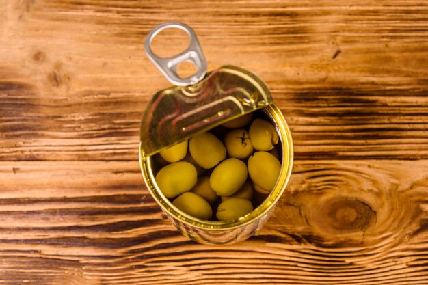 Lata abierta con aceitunas verdes sobre mesa de madera rústica. Vista superior