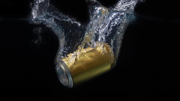 LATA DE ALUMINIO DORADO HACIENDO SALPICADURAS EN EL AGUA CON FONDO NEGRO