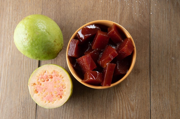 Lata amarela com geleia de goiaba cortada em cubos com goiabas ao fundo na mesa de madeira