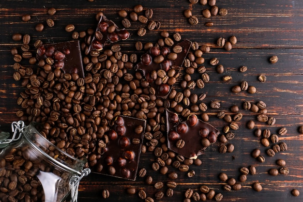 Una lata de café, granos dispersos y chocolate negro en una mesa de madera.