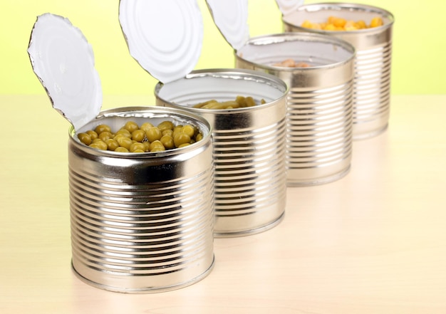 Latas abiertas de guisantes, frijoles de maíz y frijoles franceses sobre una mesa de madera sobre fondo verde