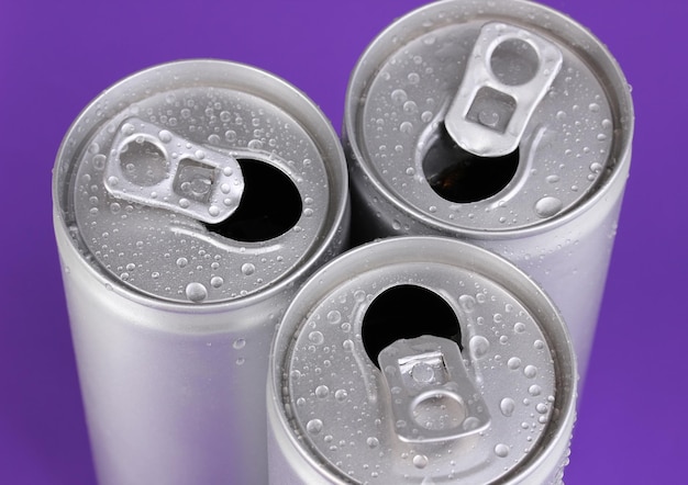 Foto latas de aluminio con gotas de agua sobre fondo morado