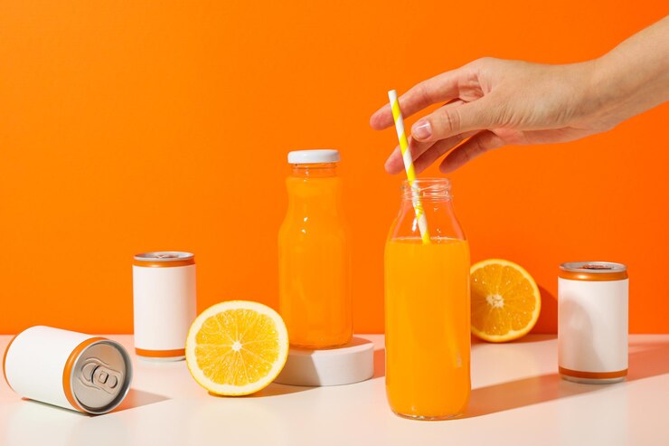 Latas, botellas de vidrio, naranjas y mano sobre fondo naranja.