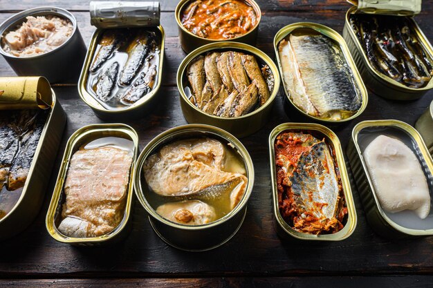 Latas de conserva abertas com Saury, cavala, espadilha, sardinha, sardinha, lula, atum sobre a mesa de madeira caseira vintage close-up vista lateral.