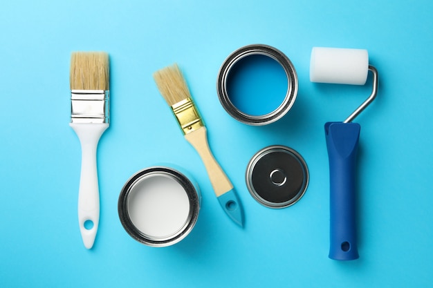 Latas de tinta, pincéis e rolo na superfície azul