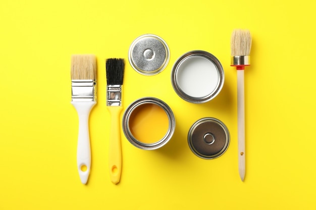 Latas de tintas e pincéis na superfície amarela