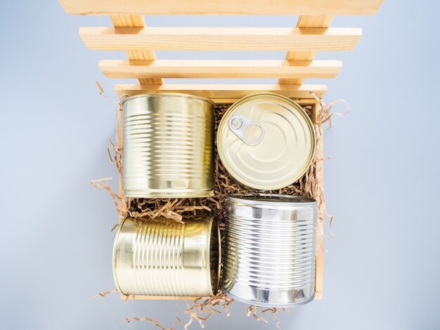 Las latas se embalan en una caja de madera con un respaldo suave, aislar sobre un fondo gris, primer plano, maqueta. Concepto de comida o regalo durante la cuarentena. Una caja de donaciones de comida, comida a domicilio.