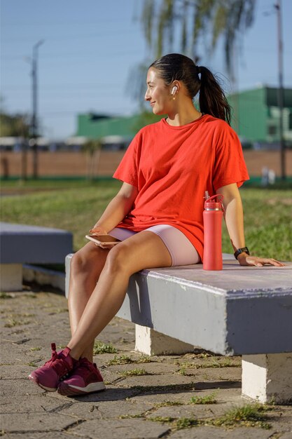 Lateinamerikanin in rotem T-Shirt sitzt auf einer Bank in einem öffentlichen Park