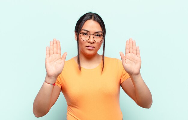 lateinamerikanische Frau, die ernst, unglücklich, wütend und unzufrieden aussieht und den Eintritt verbietet oder mit beiden offenen Handflächen Stopp sagt