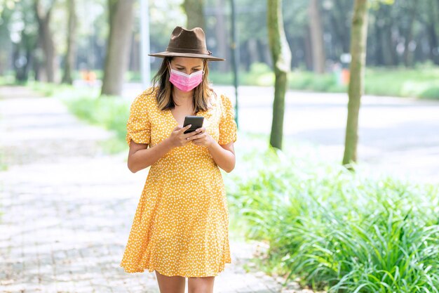 Lateinische Frau, die durch den Park geht, während sie auf ihrem Handy eine SMS schreibt