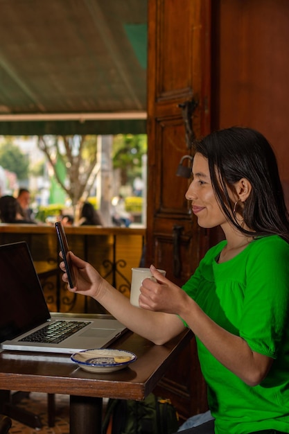 Lateinische Frau, die in einem alten Café sitzt und ihr Handy überprüft, während sie eine Tasse Kaffee trinkt