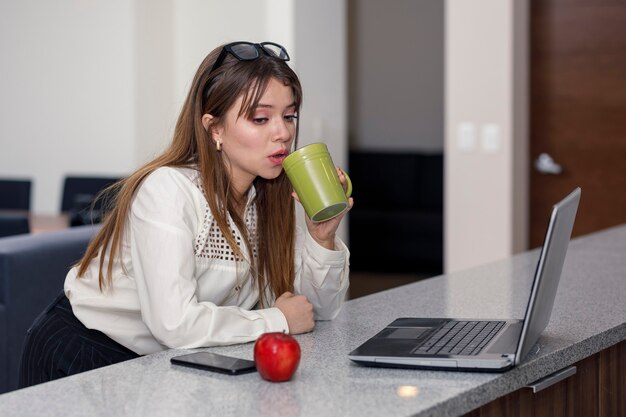 Lateinische Frau, die Kaffee trinkt, während sie an ihrem Computerkonzept arbeitet, zu Hause zu sein