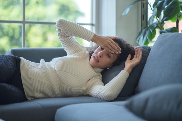 Lateinische Frau, die mit Kopfschmerzen auf dem Sofa liegt.