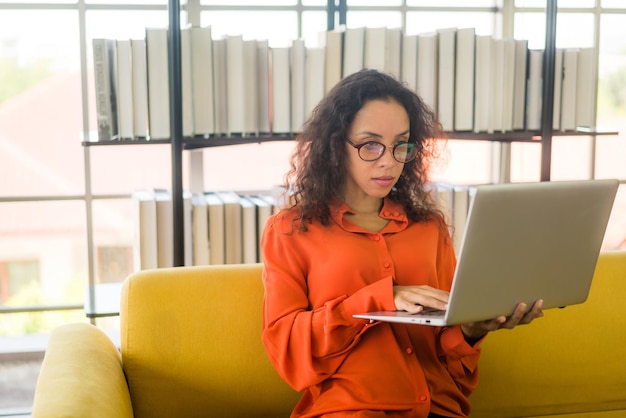 Lateinische Frau, die mit Laptop auf Sofa arbeitet