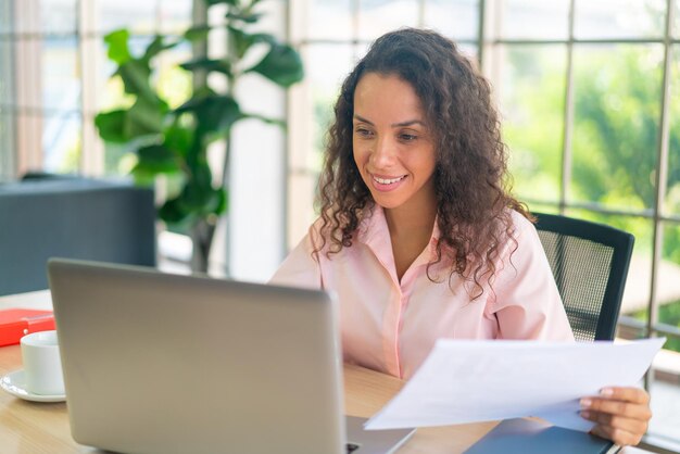 Lateinische Frau, die mit Laptop und Papier am Arbeitsplatz arbeitet