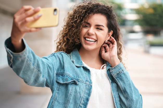 Lateinische Frau, die Selfies mit ihrem Handy macht, während sie draußen auf der Straße steht. Urbanes Konzept.