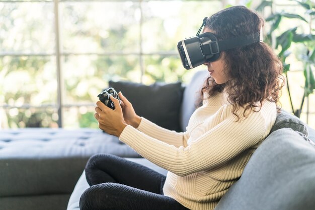 Lateinische Frau, die zu Hause ein Virtual-Reality-Headset auf dem Sofa verwendet