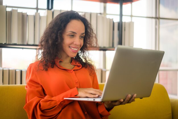 lateinische frau, die zu hause mit laptop auf sofa arbeitet