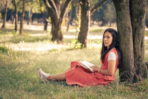 Lateinische Frau liest ein reich verziertes Buch von einem Baum im Park