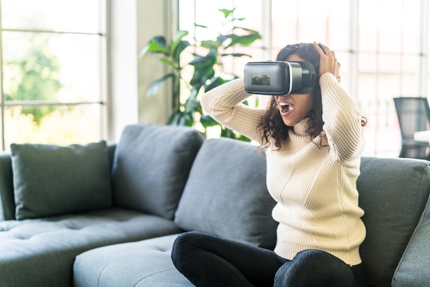 Lateinische Frau mit einem Virtual-Reality-Headset auf dem Sofa zu Hause