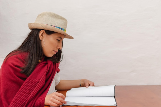 Lateinische Frau mit Hut und rotem Schal, die sitzt und ein Restaurantmenü liest