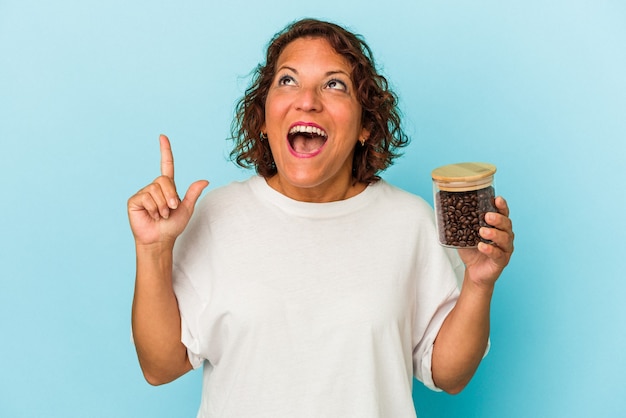 Lateinische Frau mittleren Alters, die ein Kaffeeglas isoliert auf blauem Hintergrund hält, das mit geöffnetem Mund nach oben zeigt.