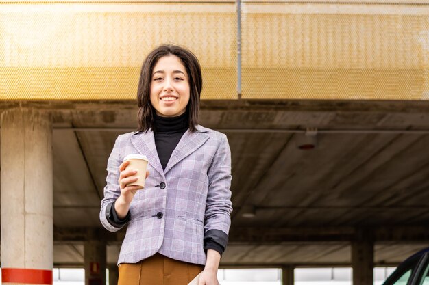 Lateinische Geschäftsfrau auf der Straße, die einen Kaffee zum Mitnehmen hält Junge Frau in der Jacke, die einen Kaffee auf der Straße hält