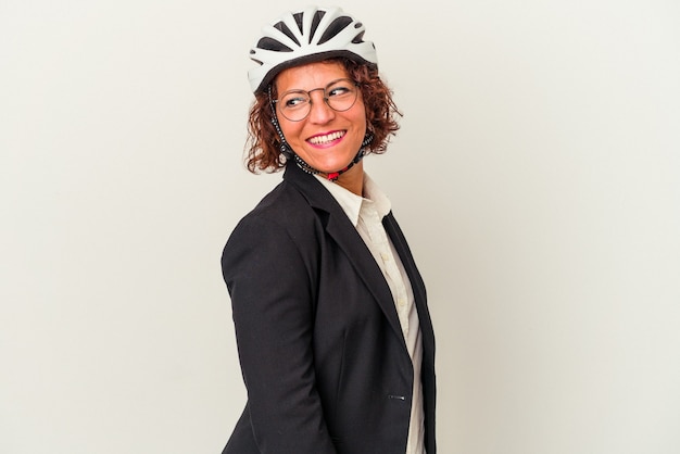 Lateinische Geschäftsfrau mittleren Alters, die einen auf weißem Hintergrund isolierten Fahrradhelm trägt, sieht beiseite lächelnd, fröhlich und angenehm aus.