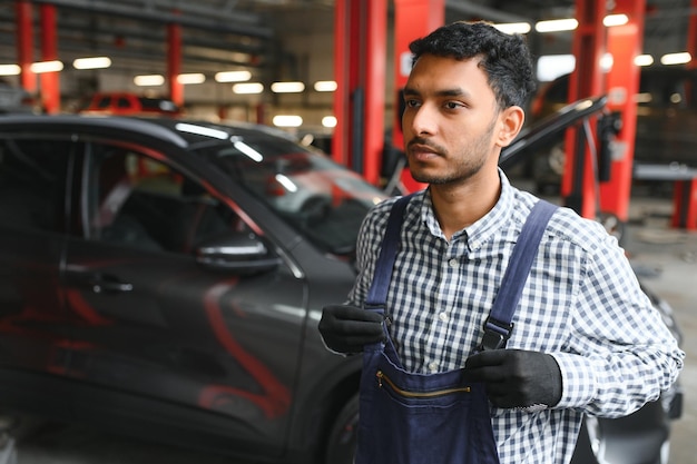 Lateinischer hispanischer Automechaniker in Uniform untersucht ein Auto, während er im Autoservice arbeitet